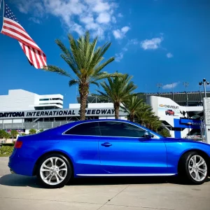 Blue Car parked in front of Daytona International Speedway and palm trees