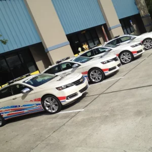 Four white cars lined in a parking lot with blue and red designs